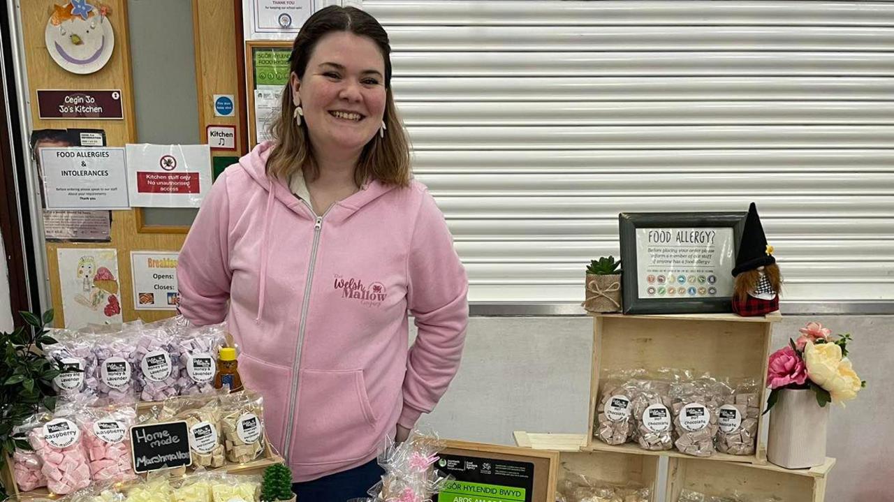 Emily Roberts stands in front of a stall of marshmallow products which she is selling, smiling