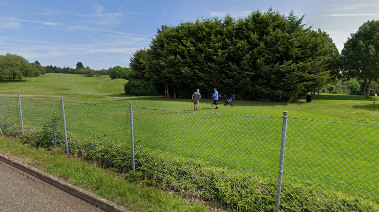 Golfers on a green grass fairway behind a mesh fence