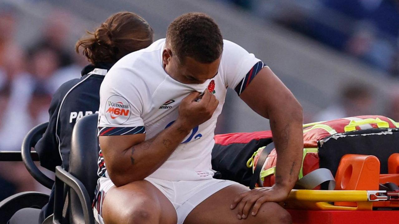 Ollie Lawrence sat on the medical car being taken off the pitch during England's game against Italy