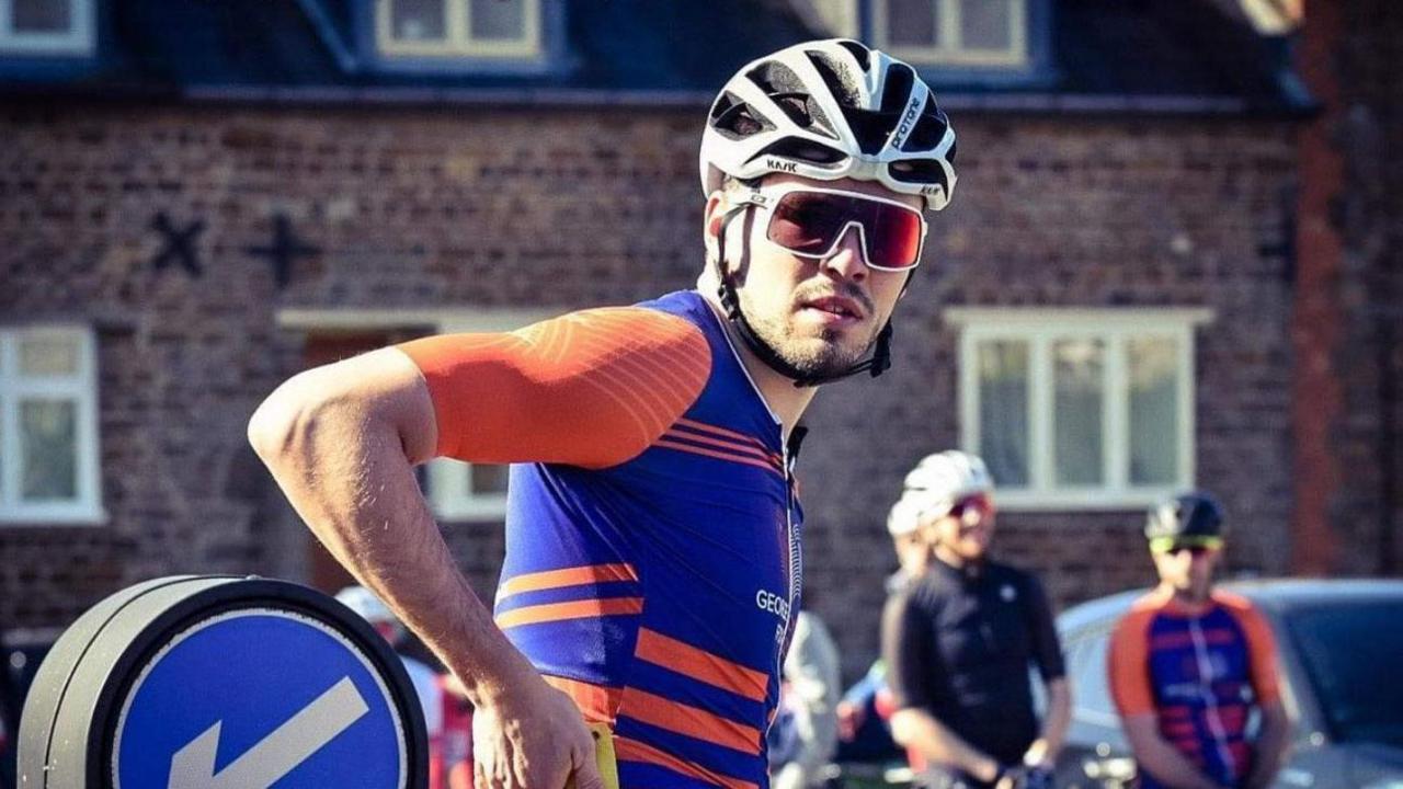 George Fox in cycling lycra which is orange and purple. He is wearing cycling sunglasses and a white helmet.