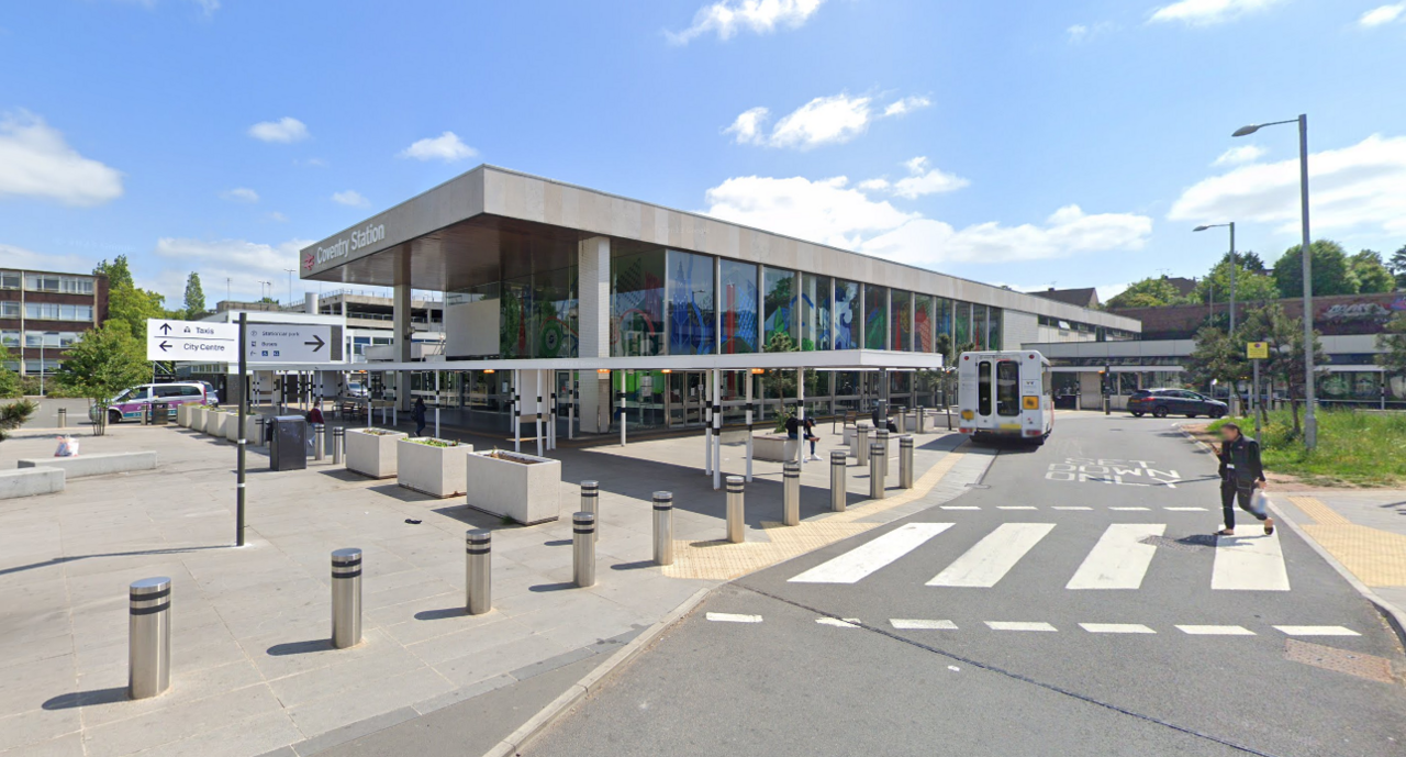 The outside of Coventry Railway Station, a two-storey, glass-fronted modernist building with an outdoor space protected from traffic by bollards. 