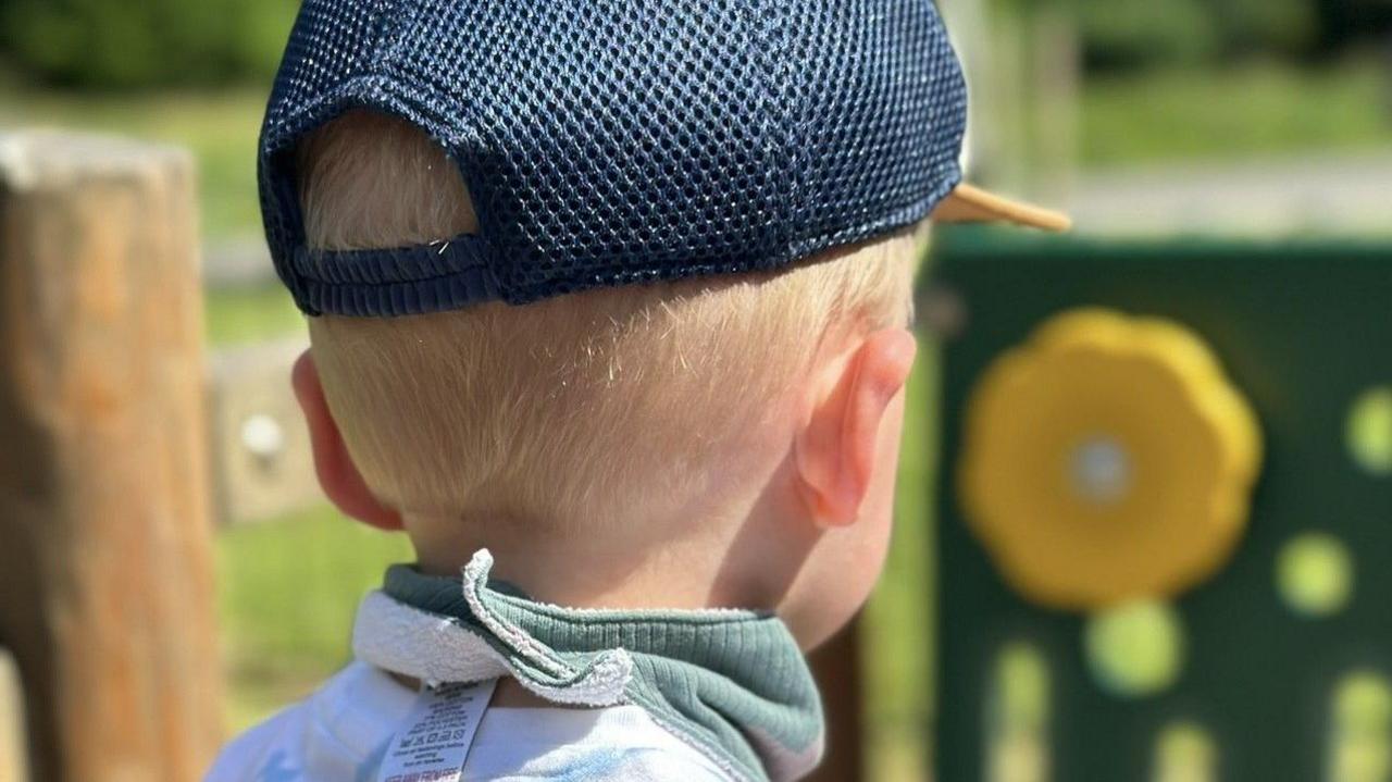 A little boy with blonde hair in a cap looking into the distance