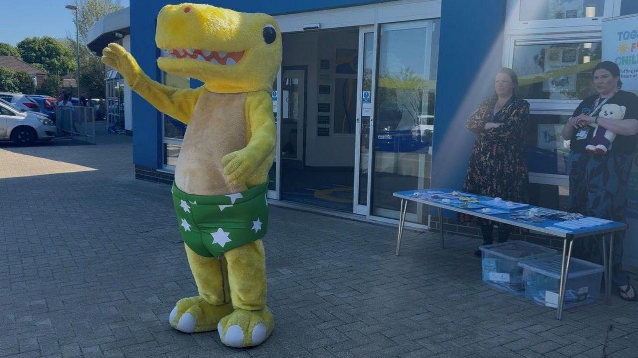 Person wearing a Pantosaurus costume, standing outside Ernesettle Community school.