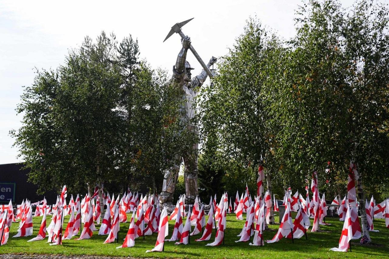 Flags are in the foreground, with trees and a statue, as high as one of the trees, in the background.