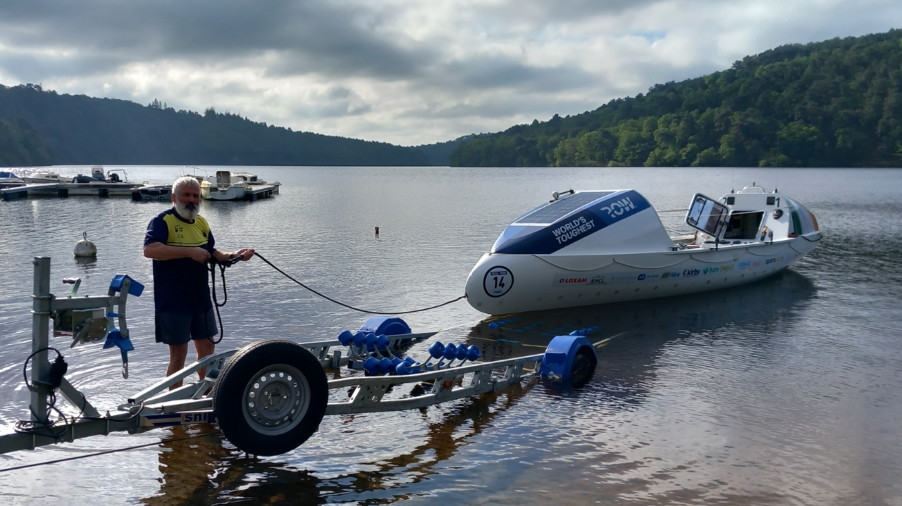 A man in a yellow and blue t-shirt holding a rope tied to a white rowing boat