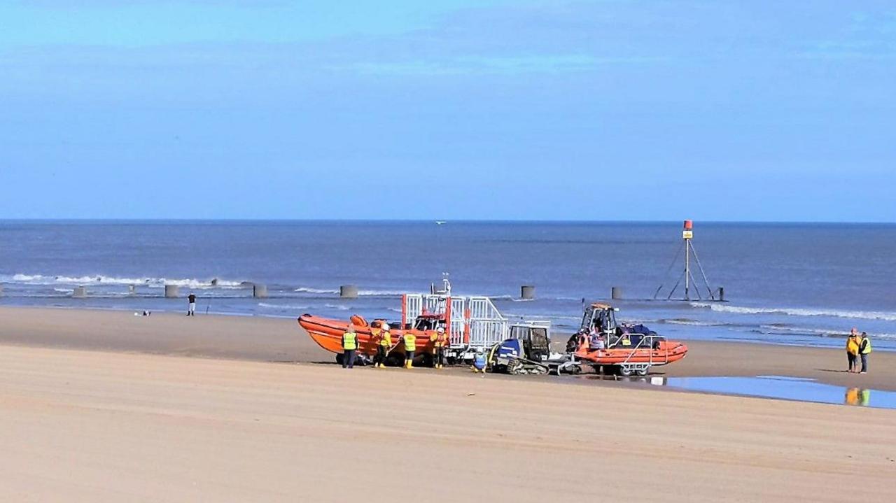 Crew members from the RNLI standing next to a brightly-coloured boat during a training exercise on the beach at Mablethorpe