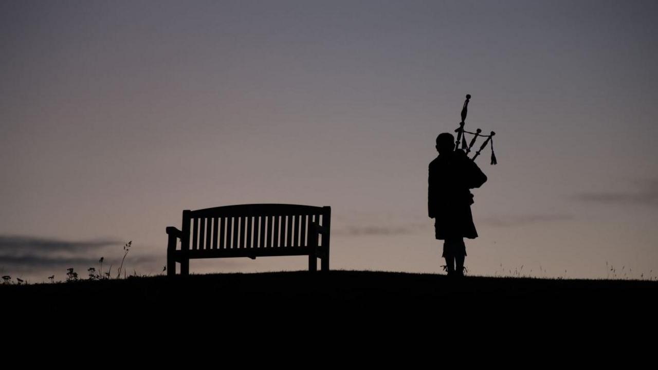 A silhouette of a bench and a piper against the night sky