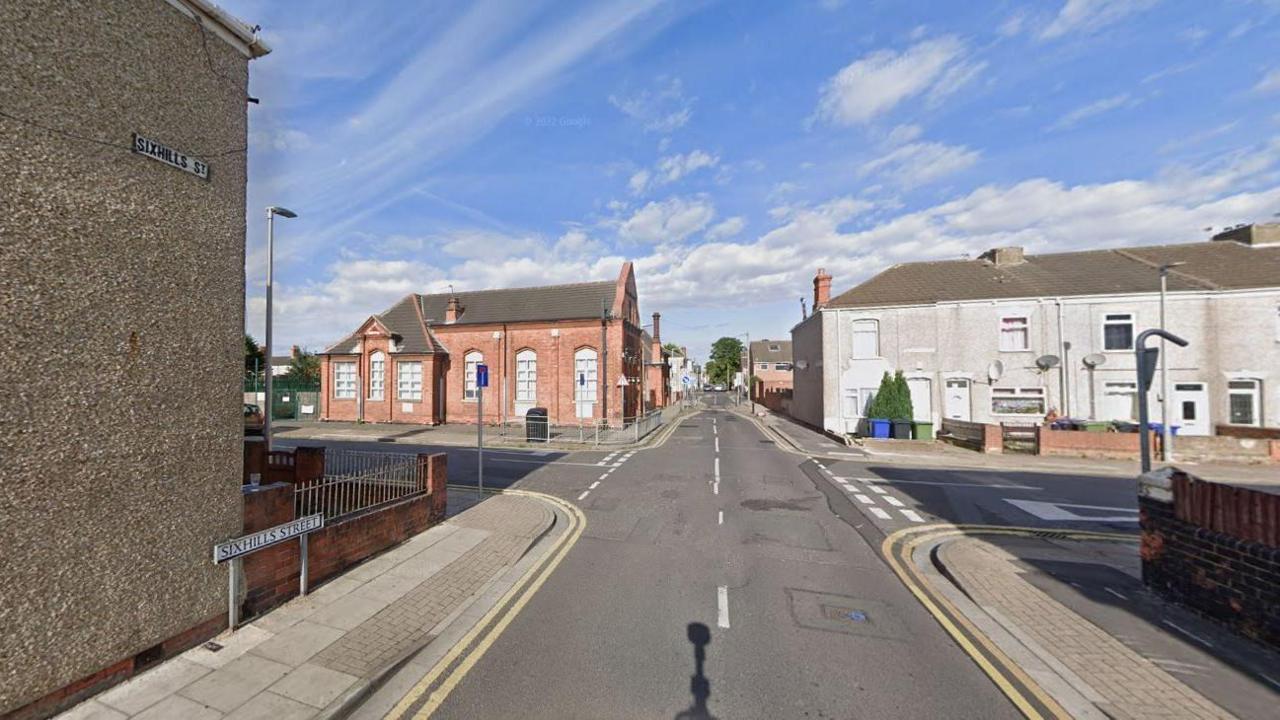 Google street view of Sixhills Street in Grimsby. The street sign can be seen on the left hand path and on the side of a house. No cars can be seen but there are terraced houses and the road extends into the distance with roads either side.