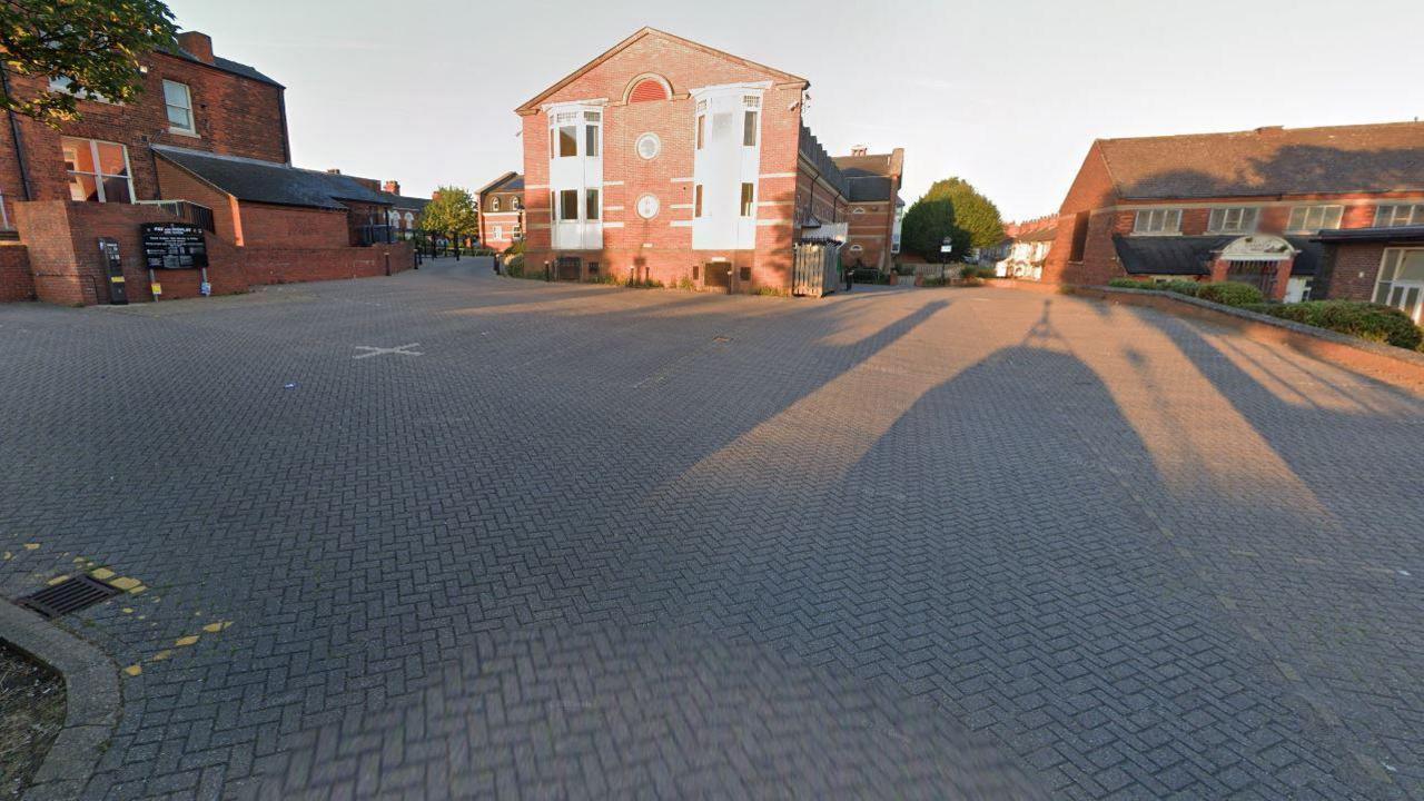 The Civic Offices building with parking spaces in front on a tiled driveway and, on a wall to the left, there is a pay and display sign and a ticket machine.