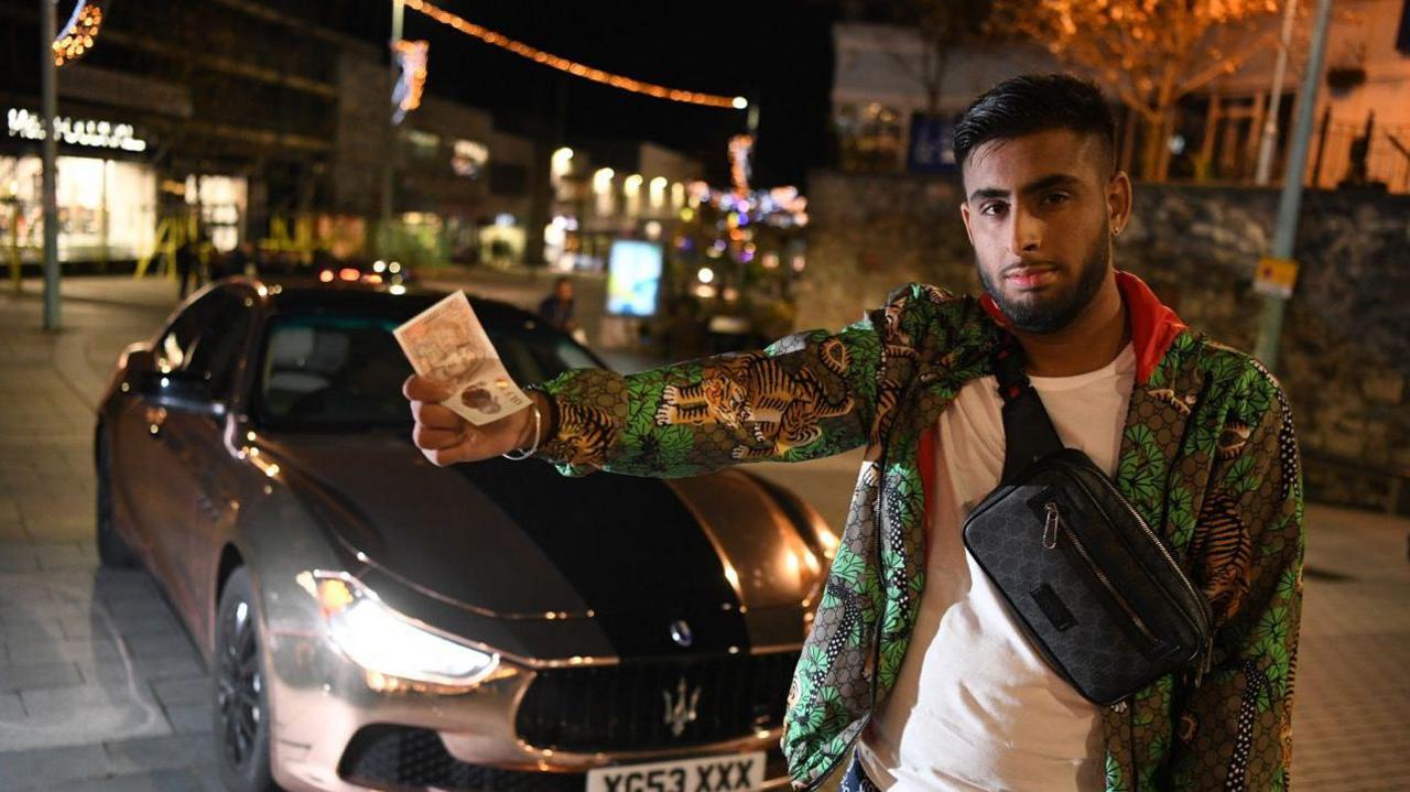 A man holding  £10 note and wearing a green jacket