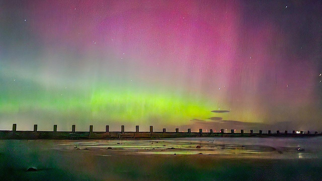 A dramatic glowing purple and green sky can be seen at night time as the northern lights illuminate the starry sky over a groin on the beach in Aberdeen with the tide out, uploaded to Weather Watchers on 12 September