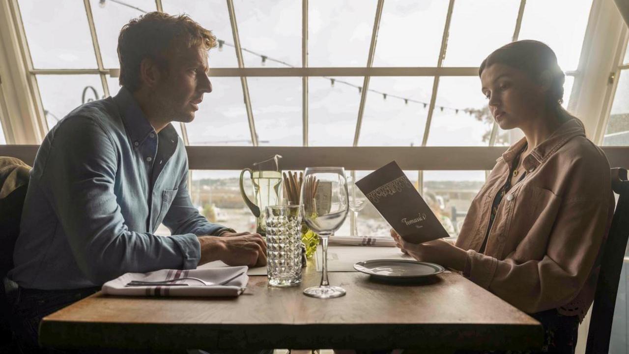 Actors Damien Molony and Chloe Sweetlove sit at a table. Chloe Sweetlove is reading the menu.