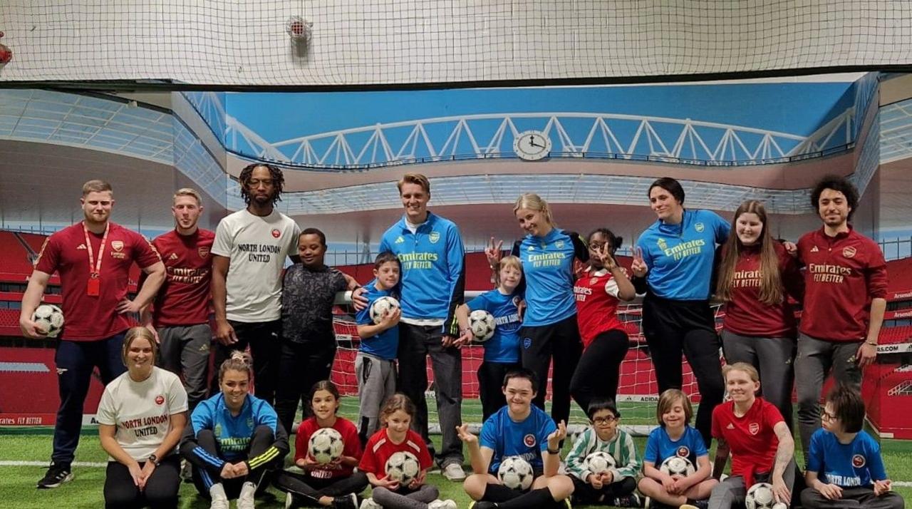 Arsenal's men's captain Martin Ooegaard and women's captain Leah Williamson OBE pose with the team, coaches and family members