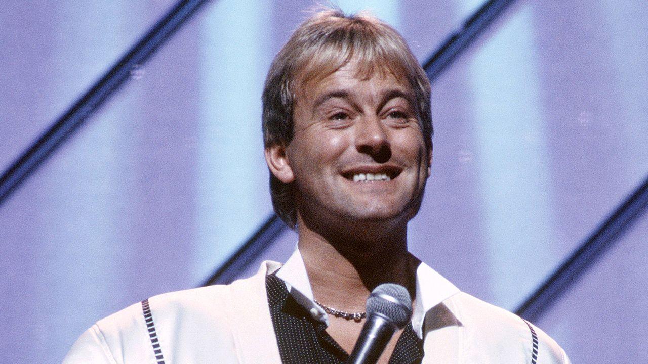 Duncan Norvelle at the London Palladium in 1987 in a white shirt holding a microphone