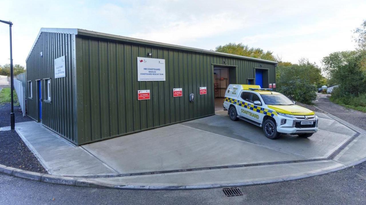 A white and yellow coastguard vehicle parked outside a green building.