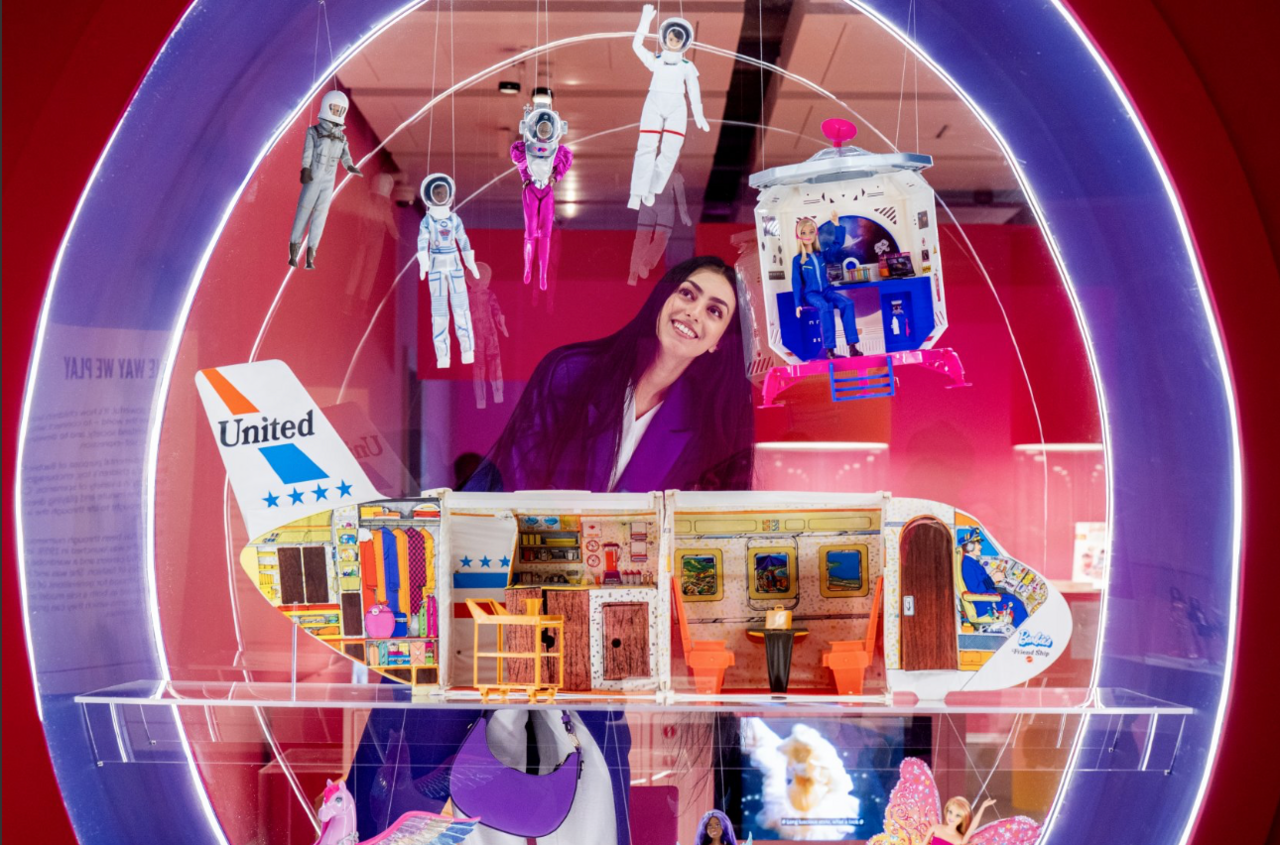 A woman with long dark hair takes a closer look at airline Barbie and space Barbie dolls on display