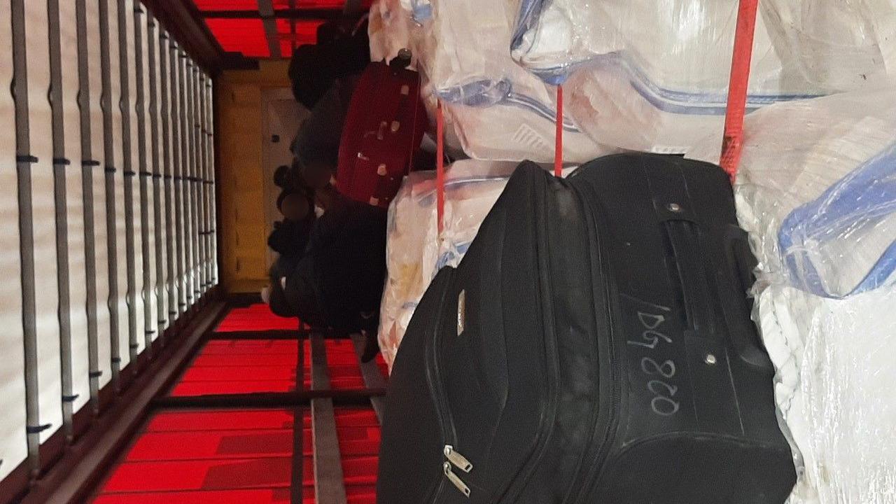 People with blurred faces in the back of a HGV trailer behind luggage and other pieces of luggage
