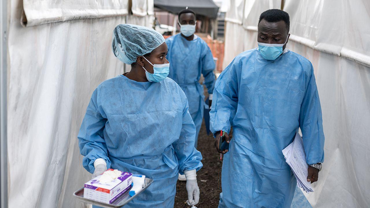 Health workers wearing masks and scrubs chat as they walk in between tents at the Munigi mpox treatment centre in North Kivu, DR Congo on 17 August