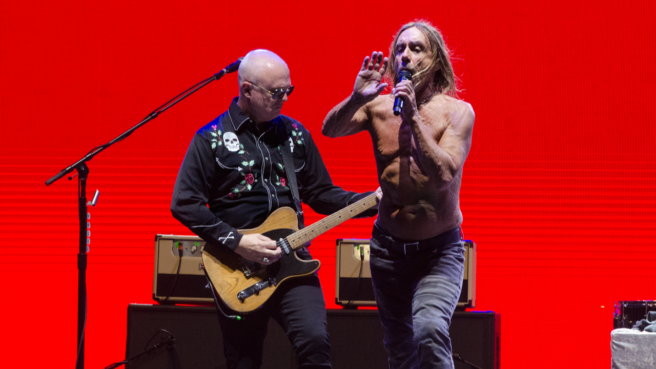 A guitarist with Iggy Pop. The pair are on stage with a red background