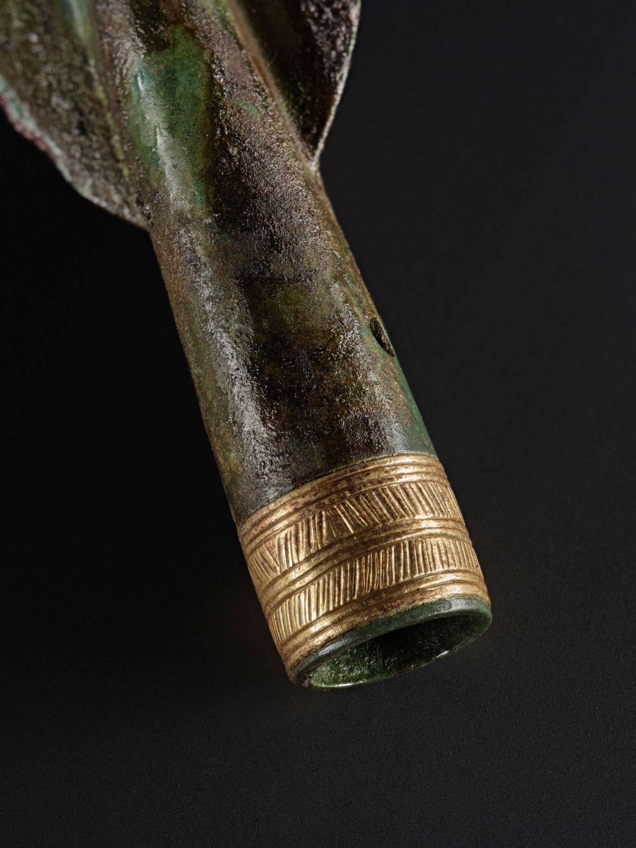 Detail of a Bronze Age spearhead with a tip decorated in gold, against a black background