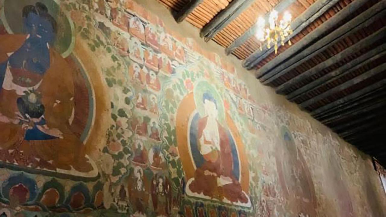 An ancient, fading mural inside the Wontoe Monastery shows Buddha seated, with other images surrounding him - the mural is painted in red, blue, green, yellow and white.   