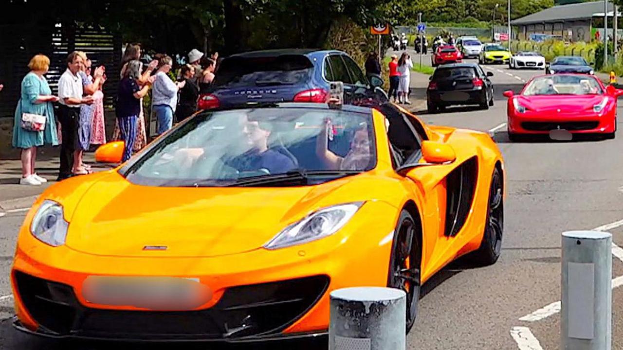 A yellow McLaren is followed by other fast cars down a road