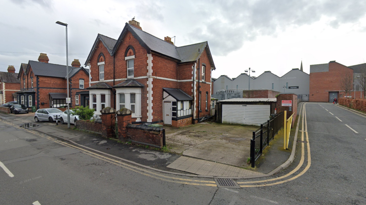 A house on a residential street. A driveway leading to the house also leads to a small garage.