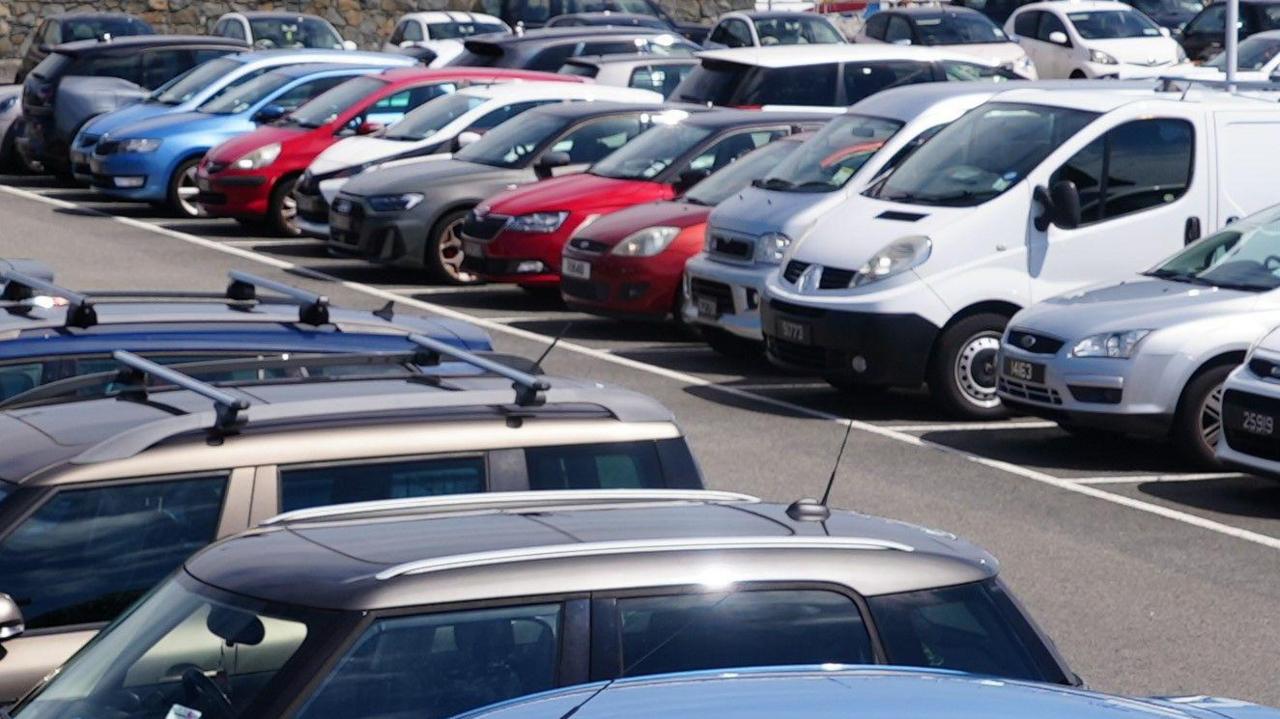 A car park with a number of parked vehicles of varying colours.