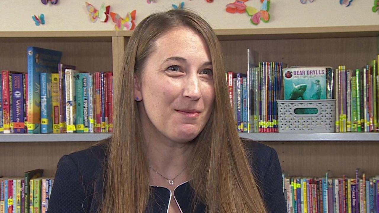 Sarah Simmons, the headteacher of Queen's Park Academy, Bournemouth, standing in the school library. A row of bookshelves is behind her.