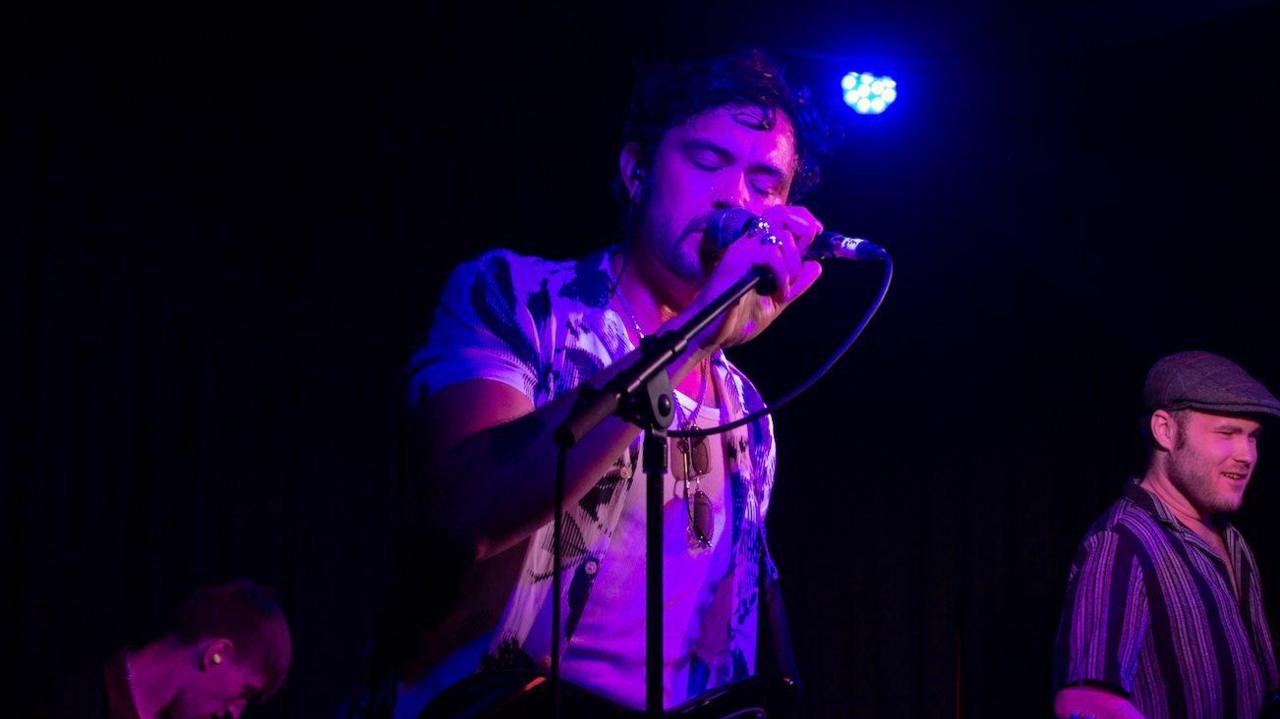 Shay Barker is holding a microphone and is lit up in purple light.