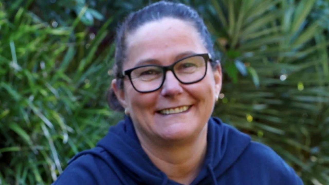 A middle-aged woman wearing glasses and with her dark hair in a pony tail smiles at the camera