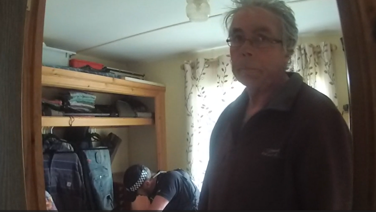 Daniel Lingham in his home as a police officer searches a cupboard behind him