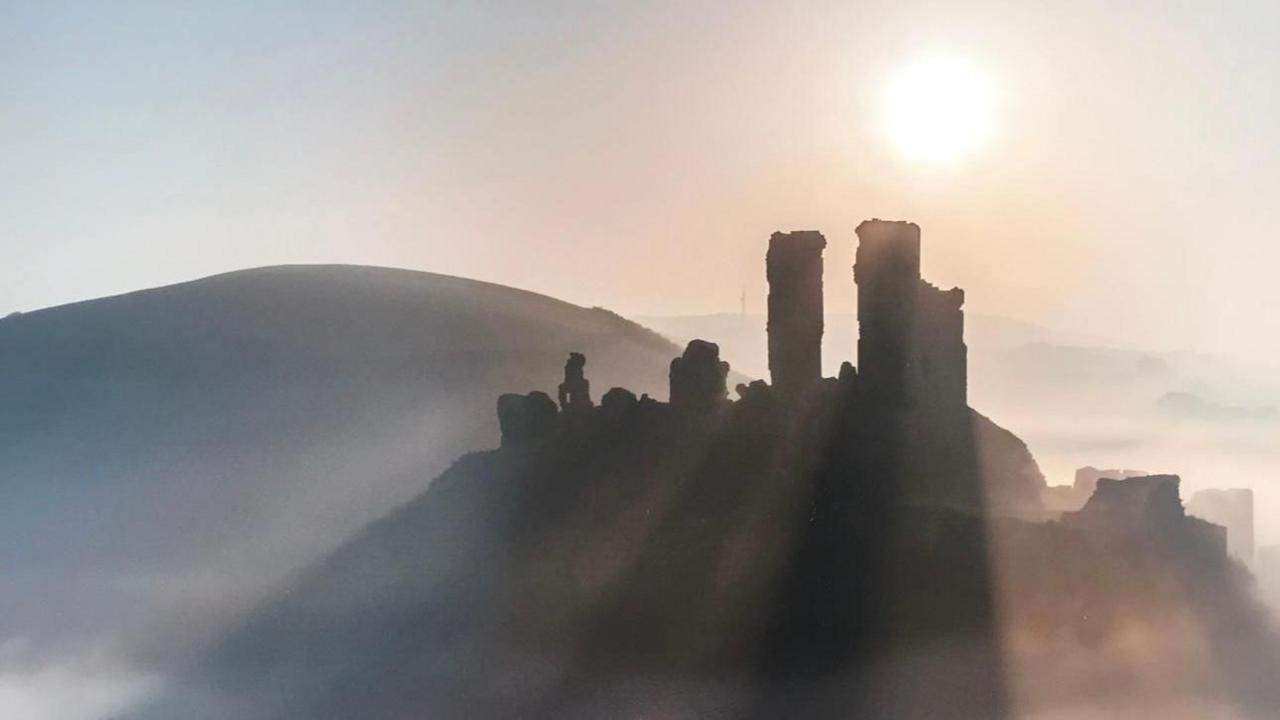 The ruins of Corfe Castle are silhouetted in mist and low sun