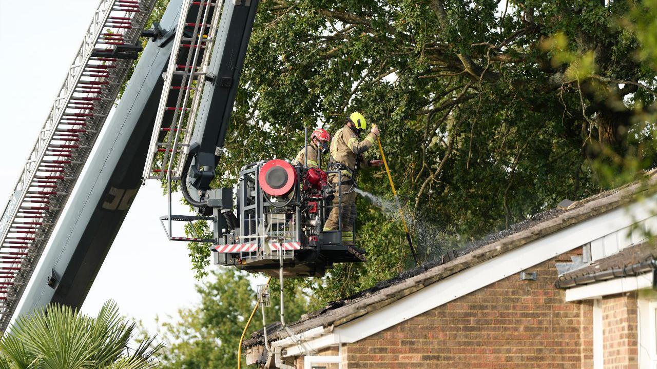 Two firefighters on a crane spray a roof of a house with water. 