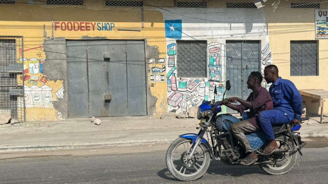 Two men on a motorbike go pass closed shops in Mogadishu