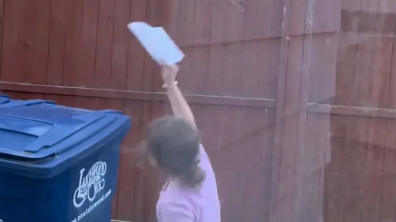 Young girl holding a paper airplane by a wooden fence