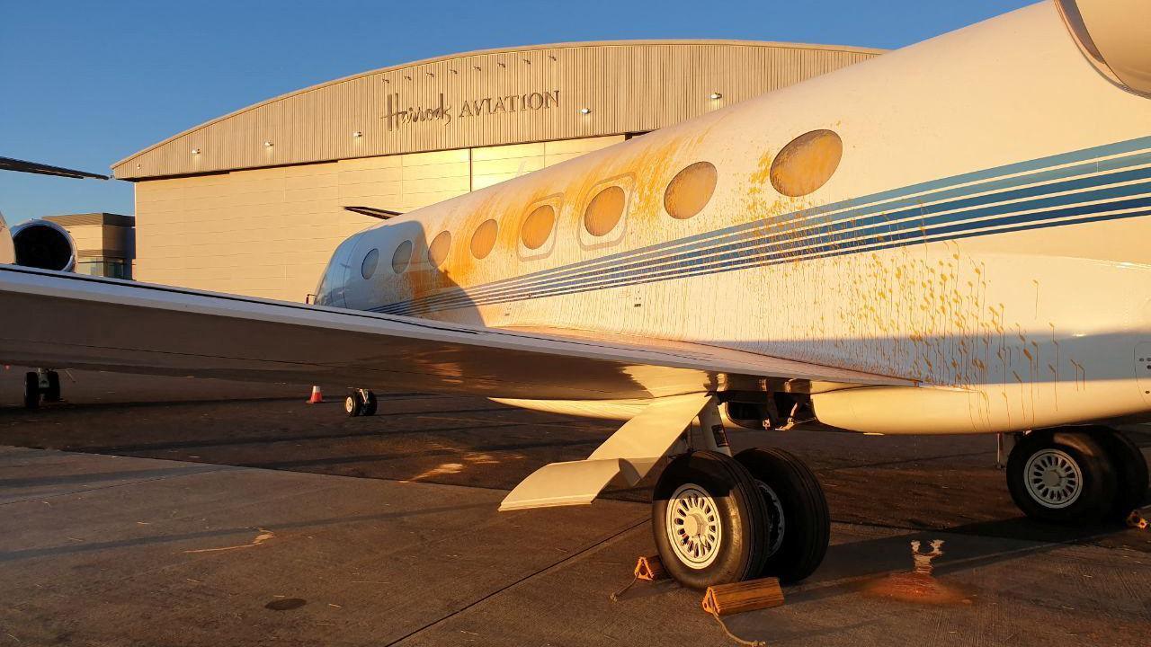 A jet sprayed with orange paint parked on a runway outside of a hangar