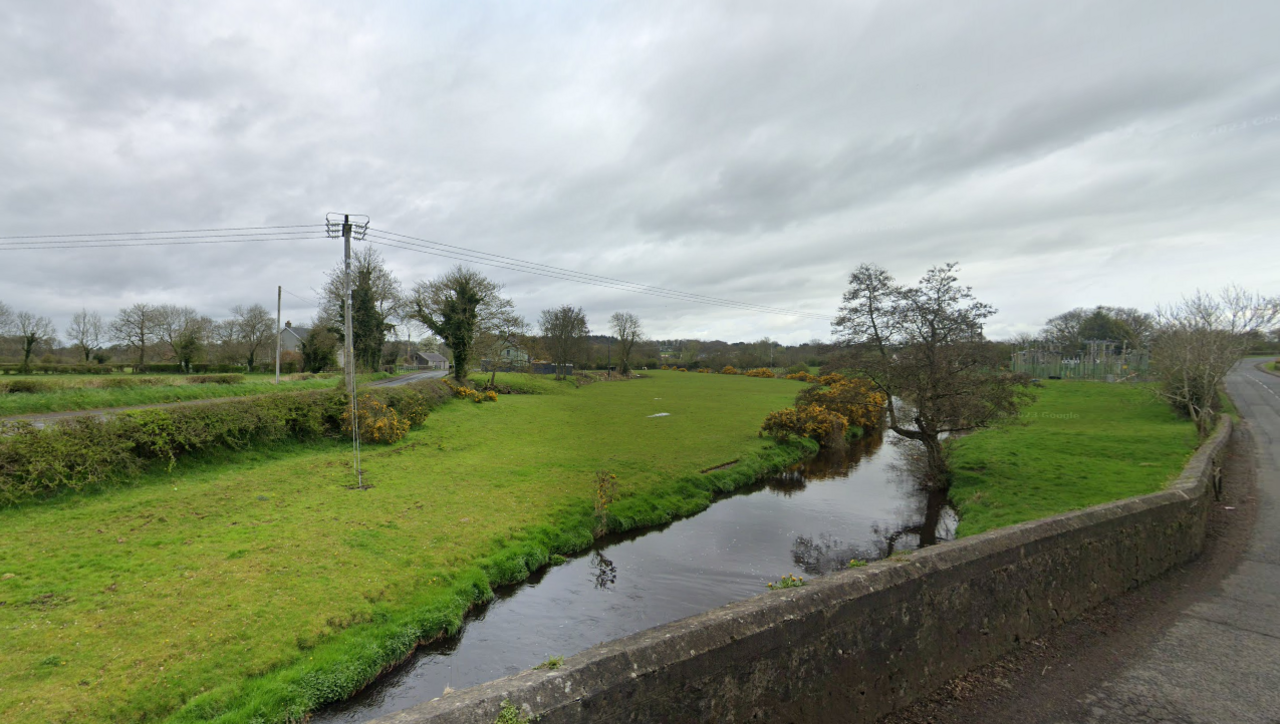 River with grass and trees on either side. In the foreground a concrete wall