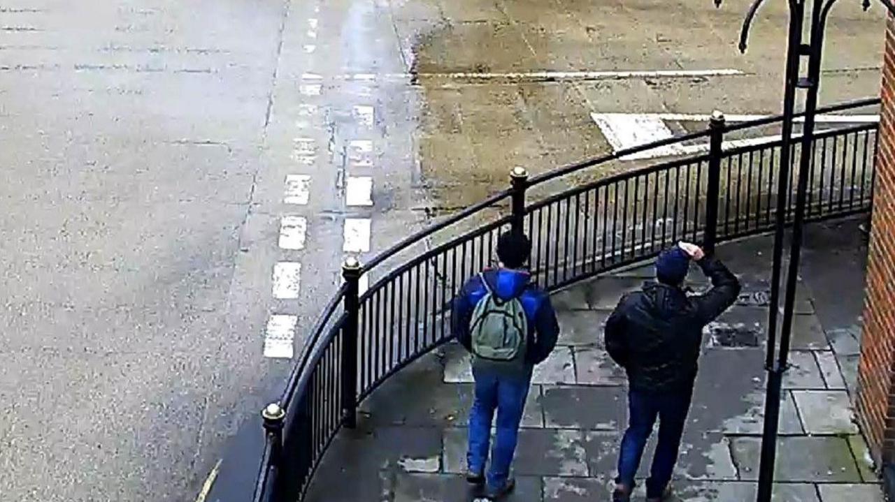 CCTV showing two men on a street corner in Salisbury, showing their backs, one wearing a grey rucksack. 