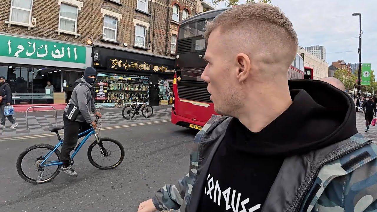 Një pamje nga videoja e Kurt Caz në Croydon, me YouTuber-in që shikon matanë rrugës drejt një çiklisti që po kalon, me dy dyqane në sfond. Teksti në anglisht i dyqanit është zëvendësuar nga tabela që duket se janë në arabisht, ndërsa çiklisti ka një balaklavë të shtuar në imazhin e tij. Imazhi i vetë Kurt Caz është modifikuar për të hequr gjestin e gishtit të madh lart që i bëri çiklistit.