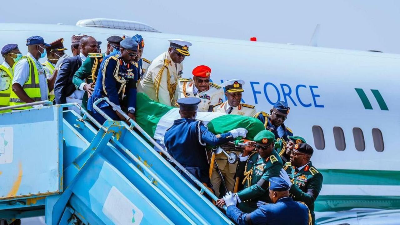 Military men - all in formal dress - carry Muhammadu Buhari's coffin down from an aeroplane.