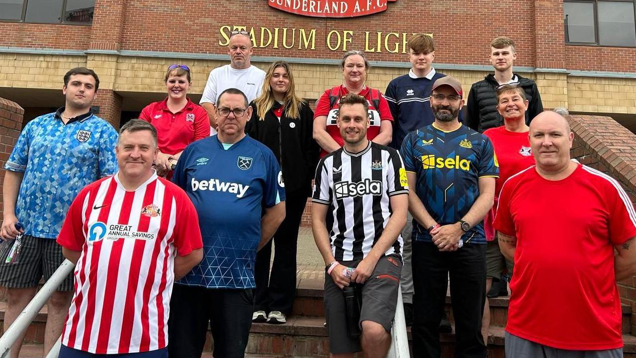 A group of people outside Stadium of Light, each wearing a different colour-ed football shirt