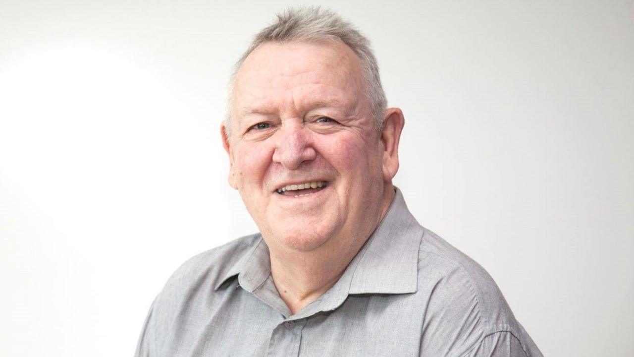 Jeff Lovell wearing a light grey shirt and smiling at the camera. He has short white hair with dark grey patches, and is sitting in front of a white background.