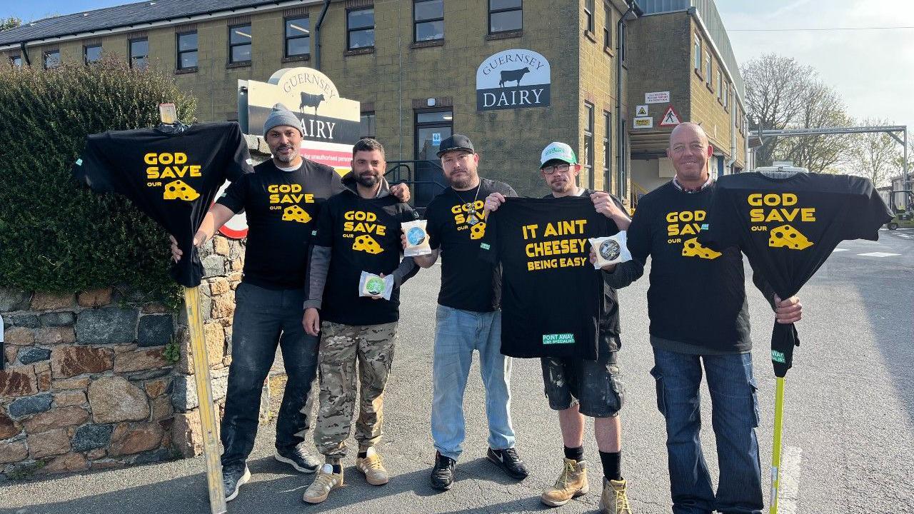 Five men wearing black T-shirts with cheese slogans written in gold lettering, standing in front of Guernsey Dairy