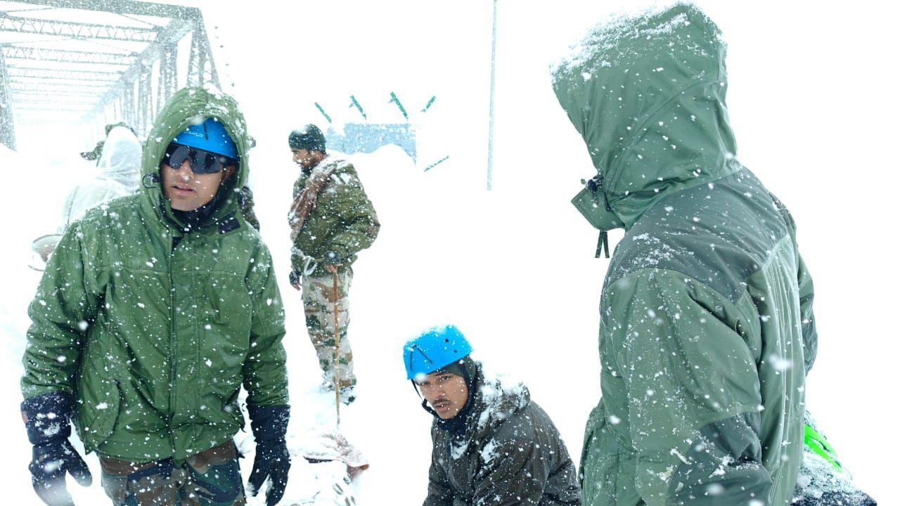 Indian army officials wearing green jackets and blue caps stand in snow as rescue operation continues 