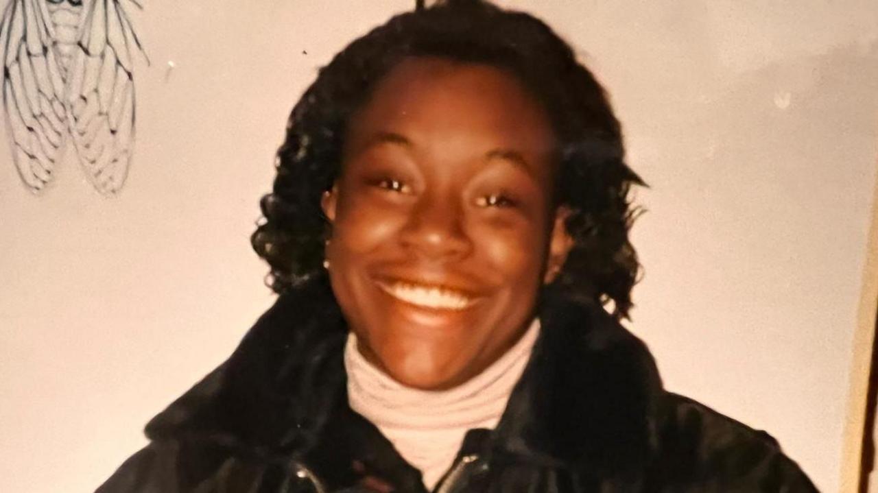 A woman with shoulder-length black hair smiling at the camera. She is wearing a black jacket.