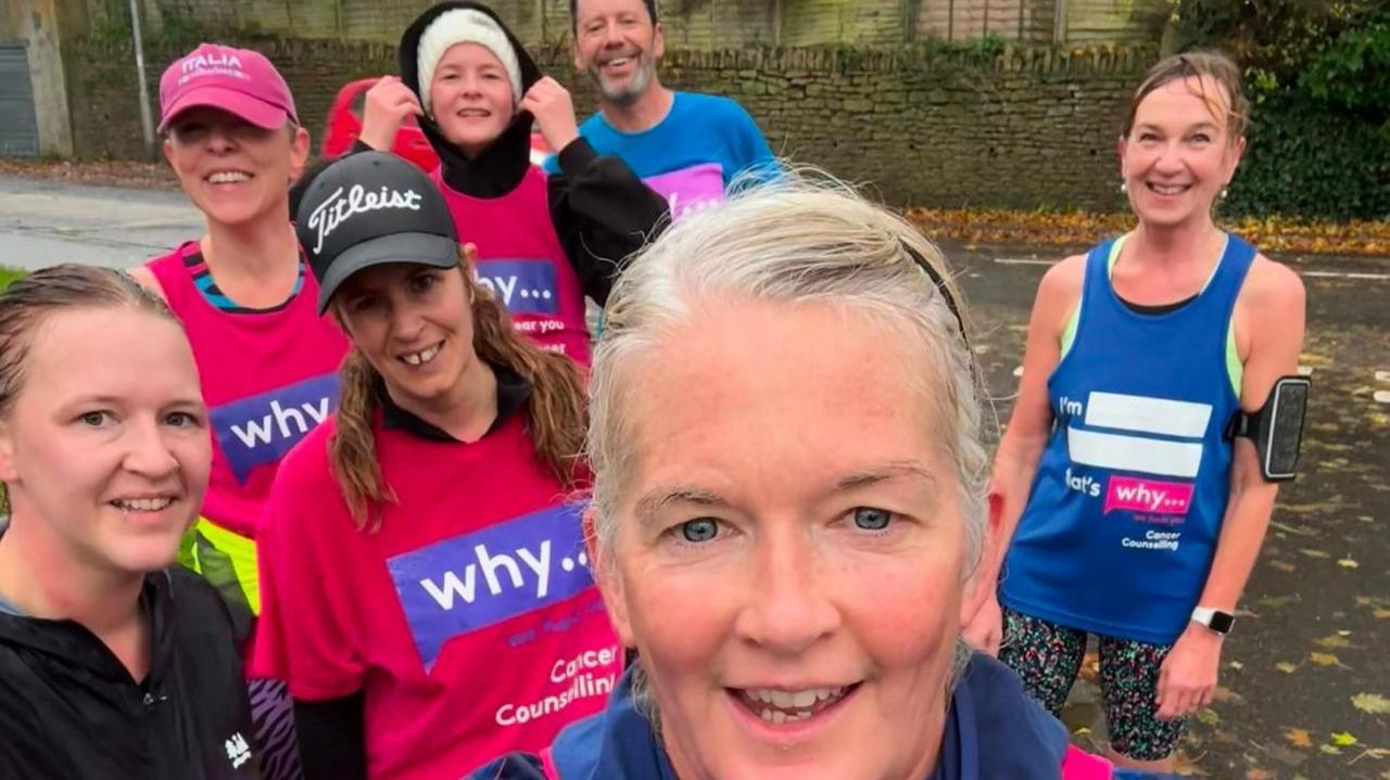 Rachel Clark and a group of runners. They are all pictured outside, wearing running gear and T-shirts with the WHY... logo on the front. All of them are looking at the camera and smiling. 