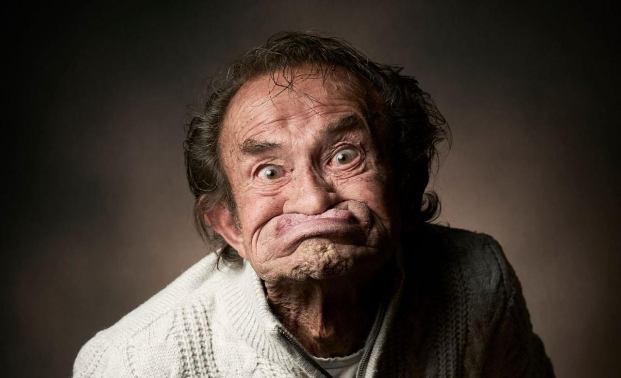 Mark McCormack gurns. He has blown his mouth out and pulled his lips up under his nose, and is staring intently at the camera