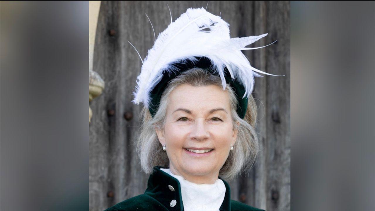 Amy Crawfurd with long, light-coloured hair wearing a large ceremonial hat with feathers