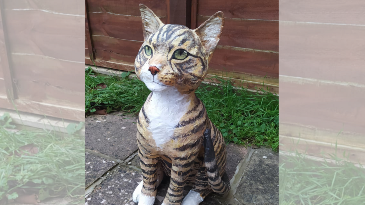 A sculpture of a cat made out of newspaper and tinfoil, in a garden